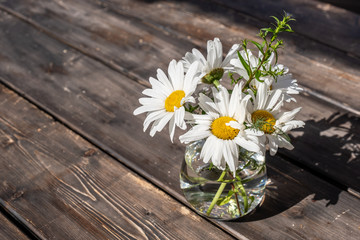 bouquet of white daisies in a glass vase on a wooden table