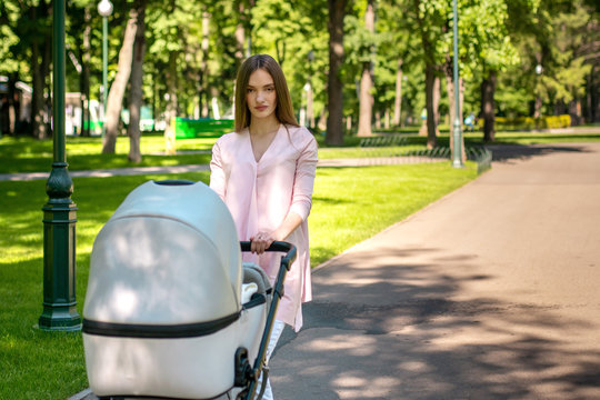 Young Mom Walks With Stroller In The Park