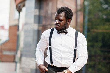 Handsome fashionable african american man in formal wear, bow tie and suspenders, walking stick.