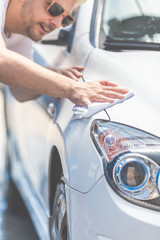 Modern young man cleaning car with cloth, car maintenance and car wash concept.