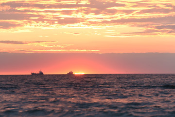 Dawn at the sea. The sun is rising over the horizon and the silhouettes of ships on the horizon. soft selective focus.