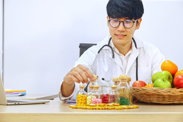Asia nutritionist pick up supplyment bottle on working table which have group of fruits in the basket