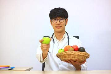Nutritionist show green apple on his hand and sit on working table which have labtop and group of fresh fruit , helathy diet concept.