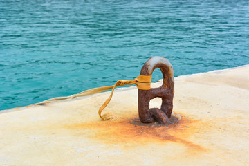 Sea, concrete, metal. Light yellow sea pier with a large rusty loop and turquoise sea.