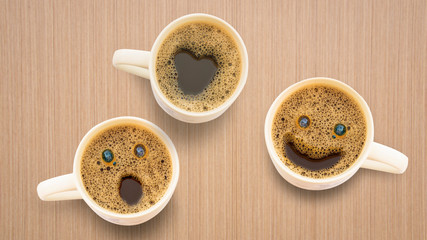 Three different faces coffee cup on a wooden table.