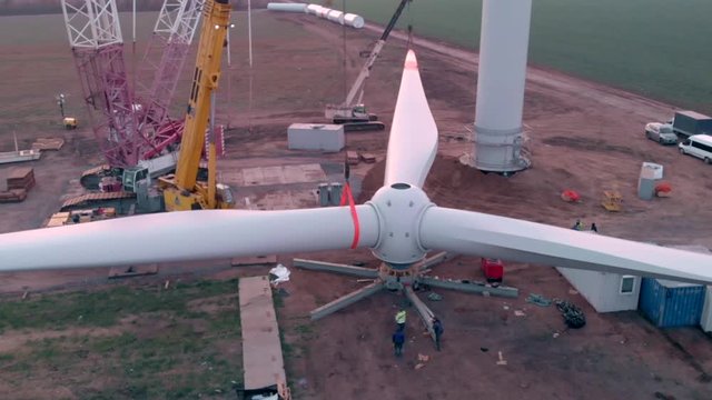 Building process of wind energy power tower mill, under construction. Assembling blades, turbine, rotor. Green, clean, renewable energy. Aerial footage.