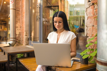 Attractive woman in glasses prosperous marketing coordinator accounting via pc laptop computer, sitting in coffee shop. Hipster girl online shopping store via notebook while relaxing in restaurant