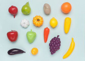  Toy plastic imitations (fake) of different vegetables and fruits on a blue background. Visual...
