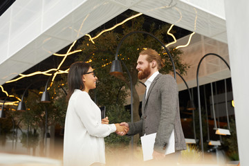 Young business couple standing and shaking hands they greeting each other before business meeting near the restaurant © AnnaStills