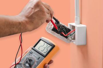 Electrician is using a digital meter to measure the voltage at the power outlet  isolated on orange color pastel background, with clipping path.