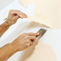 Close-up view on hands with a scraper in the process of removing wallpaper.