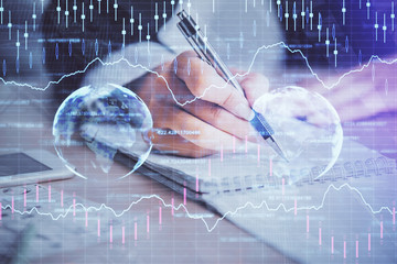 A woman hands writing information about stock market in notepad. Forex chart holograms in front. Concept of research. Multi exposure