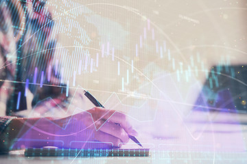 A woman hands writing information about stock market in notepad. Forex chart holograms in front. Concept of research. Double exposure