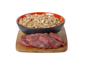 Sprouted wheat porridge in red and black bowl with raw beef meat near it. On wooden desk. Isolated on white background. Idea for healthy diet meal.