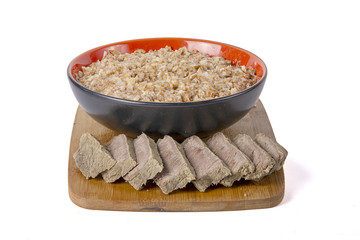 Sprouted wheat porridge in red and black bowl with sliced boiled chicken meat near it. On wooden desk. Isolated on white background. Idea for healthy diet meal.