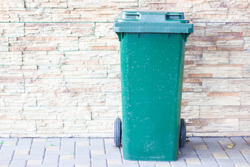 green trash can on the street near the light stone wall of the house