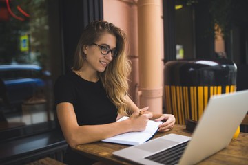 Happy smiling woman in glasses successful business owner having online video conference via laptop computer, sitting in coffee shop. Cheerful female having online webinar via netbook gadget