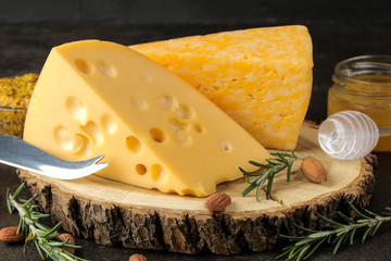 Slices of delicious marbled cheese and Maasdam cheese with honey, rosemary and mendal on a dark background