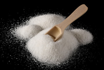 Sugar crystals, pile with wooden spoon isolated on black background