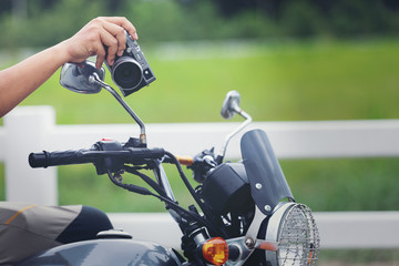 Young Asian male traveler and photographer sitting on the classic style racer motorbike holding camera  taking photo on road ,Travel photography concept