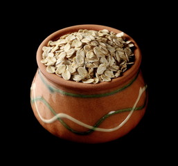 Oats, grain cereal in clay pot isolated on black background