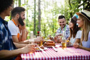 Group of happy friends eating and drinking beers at barbecue dinner