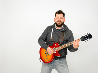 cool man with black hair and beard, wearing grey hoodie playing the electric guitar in front of a white background and havin fun