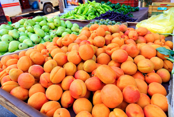 Apricots, pears, peppers, plums are on the market counter for sale.