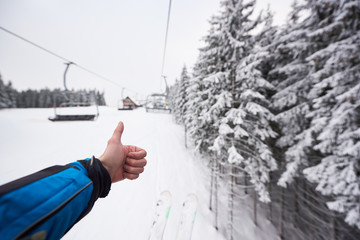 Point of view with male's hand with thumb up for snowy nature forest around ski lift. Unrecognizable man on ski lift. Cropped photo of skier hand, amazing monochrome mountain hill blurred view. POV