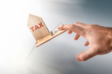 The concept of Bank investments and risks. A man's hand falls into a mousetrap, with a cardboard insert with the text TAX