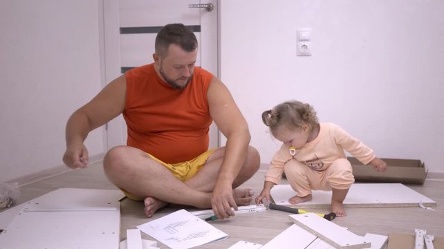 Nice chubby Father with beard and baby daughter are assembling a wardrobe bed at home. The furniture is white. happy family concept