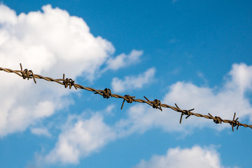 Barbed wire on the blue sky with clouds background.