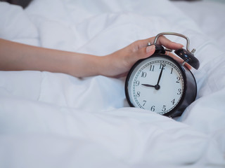 hand holding alarm clock on the bed