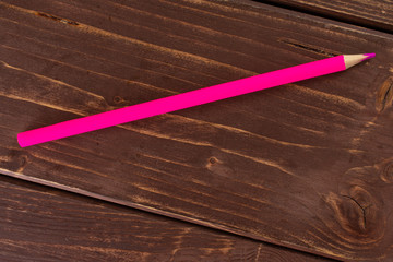 One whole pink colored pencil flatlay on brown wood