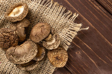 Lot of whole dry mushroom shiitake on jute cloth flatlay on brown wood