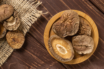 Lot of whole dry mushroom shiitake on bamboo plate on jute cloth flatlay on brown wood