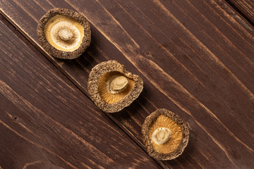 Group of three whole dry mushroom shiitake in row flatlay on brown wood