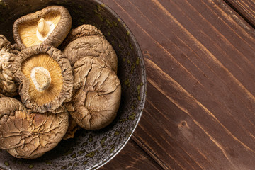 Lot of whole dry mushroom shiitake on grey ceramic plate flatlay on brown wood