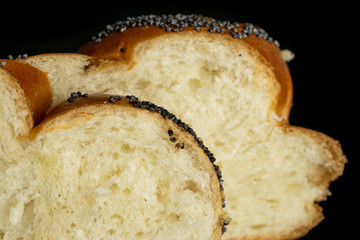 Closeup of two slices of twisted poppy seed bun isolated on black glass