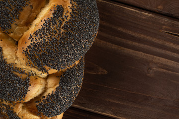 One whole twisted poppy seed bun flatlay on brown wood
