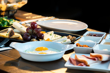 Breakfast with fried egg, cheese plate, vegetables honey and cream and marmalade on wooden table