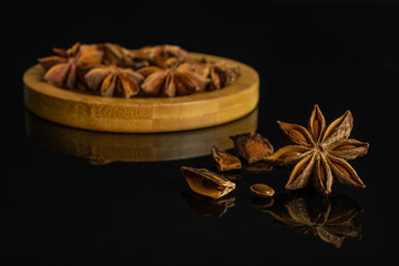 Group of lot of whole four pieces of dry brown star anise illicium verum on round bamboo coaster isolated on black glass