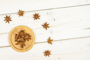 Lot of whole dry brown star anise illicium verum on round bamboo coaster flatlay on white wood