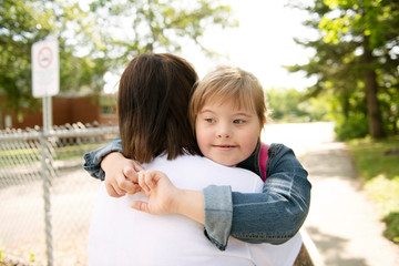 A portrait of trisomie 21 child girl outside hugging his mother on a school playground