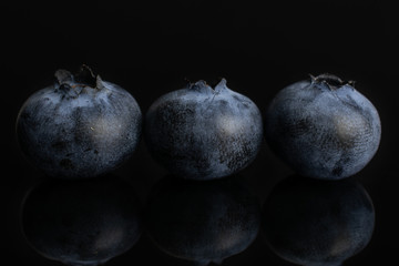 Group of three whole fresh blue bilberry isolated on black glass