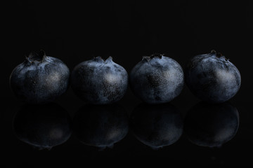 Group of four whole fresh blue bilberry isolated on black glass