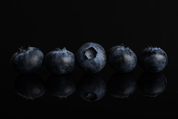 Group of five whole fresh blue bilberry isolated on black glass