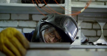 Close-up portrait of a welding master-a man in gloves and a helmet working with a detail that cooks, collects it.