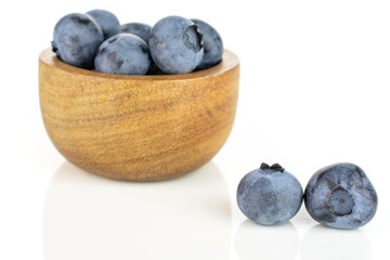 Lot of whole fresh blue bilberry in tiny wooden bowl isolated on white background