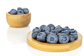Lot of whole fresh blue bilberry in tiny wooden bowl on round bamboo coaster isolated on white background